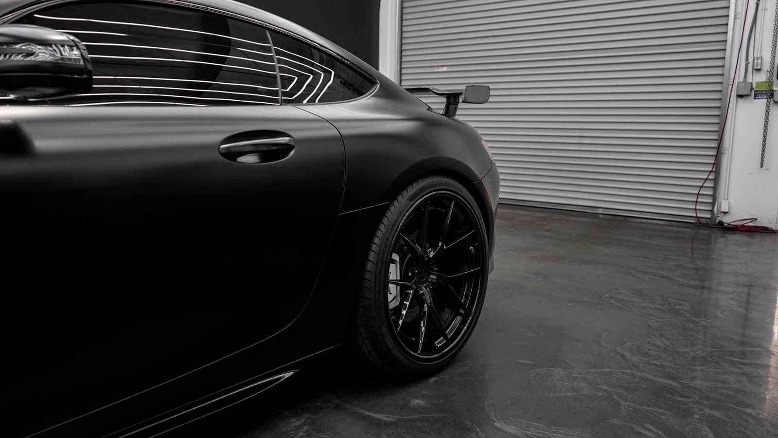 Une voiture noire aux reflets mats devant la porte d’un atelier automobile