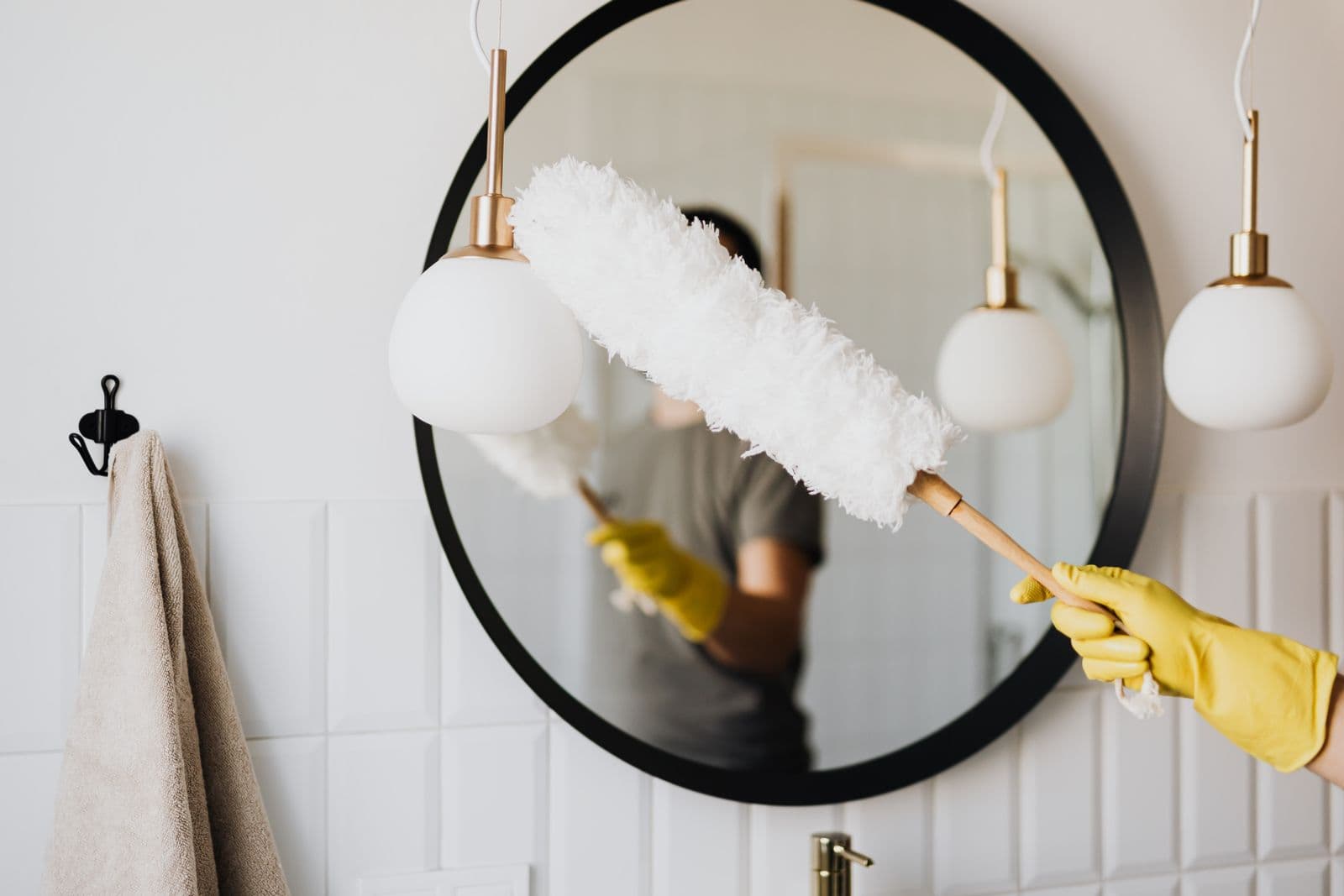 Une personne nettoie un miroir avec un plumeau et des gants jaunes